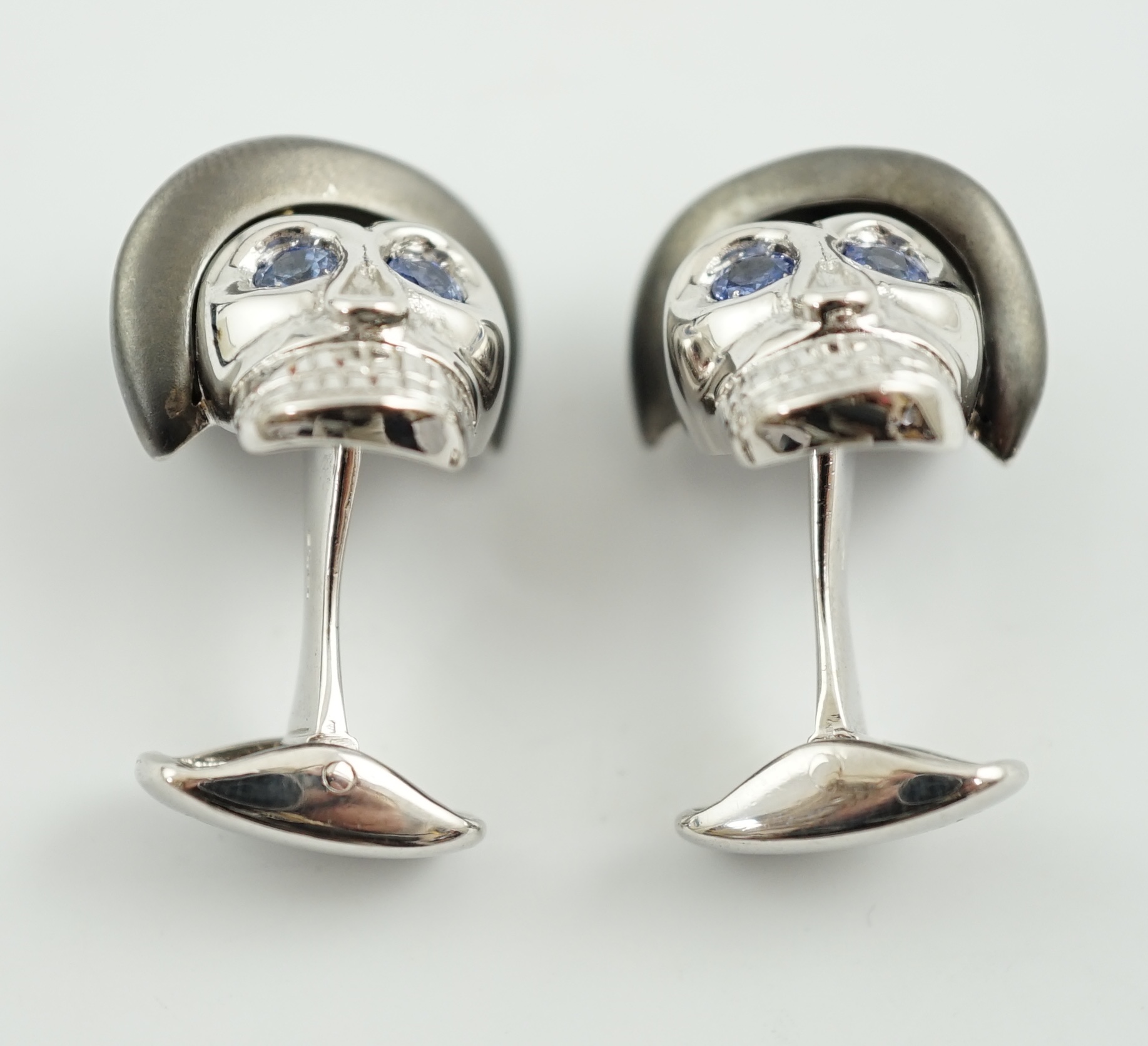 A modern pair of Longmire 18ct white gold, blackened rhodium and sapphire set novelty cufflinks, each modelled as a skull wearing a bowler hat